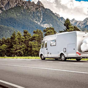 Wohnmobil fährt auf Landstraße vor Alpenkulisse, ideal für Camping und Reisen in der Natur.