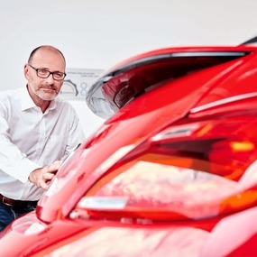 Mann prüft an rotem Auto die Heckklappe bei Gebrauchtwagenbewertung im Autohaus.