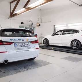 Zwei weiße BMW werden in einer modernen Kfz-Werkstatt auf einer Hebebühne geprüft.