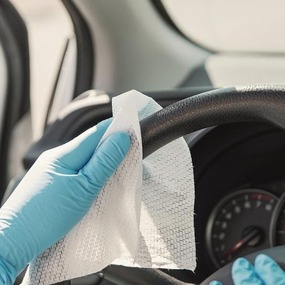 Mit Einmalhandschuhen wird das Lenkrad im Auto mit einem Desinfektionstuch gereinigt.