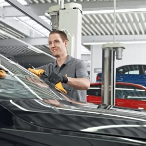 Automechaniker reinigen Windschutzscheibe in moderner Werkstatt für Fahrzeugpflege.