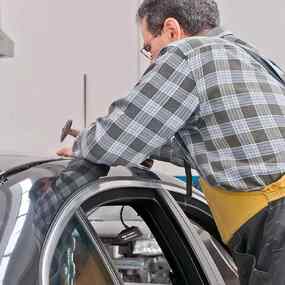 Ein Automechaniker repariert eine Delle im Autodach in einer Kfz-Werkstatt.